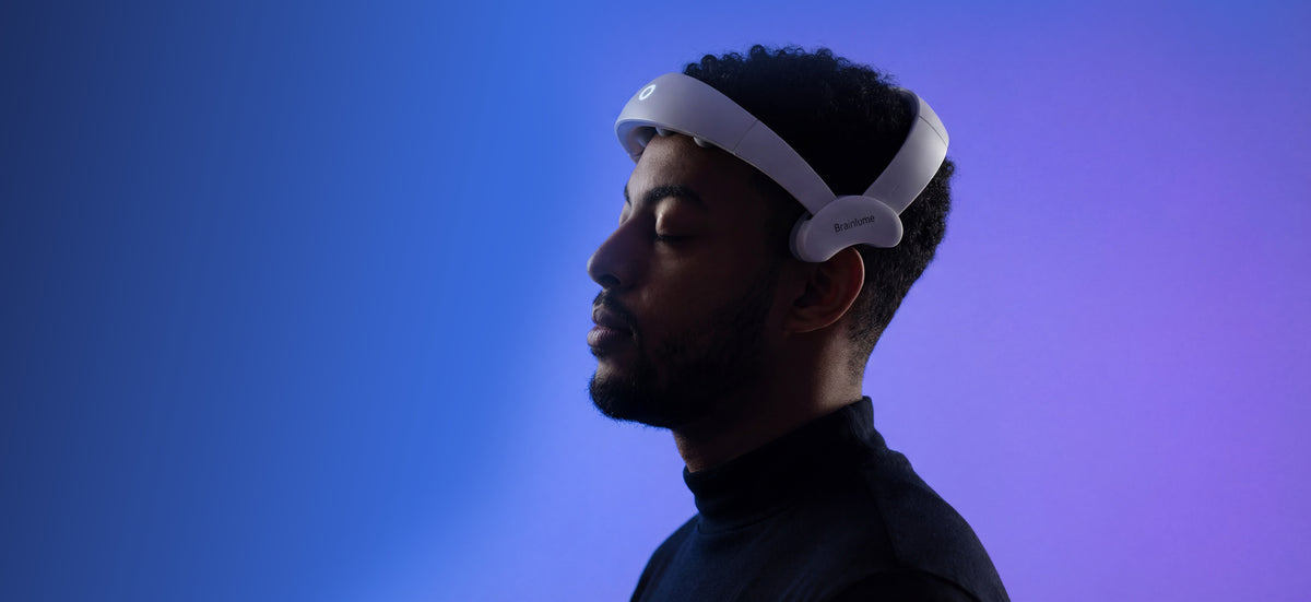 A man in profile wearing a white brianlume device, shown against a blue-to-purple gradient studio background.